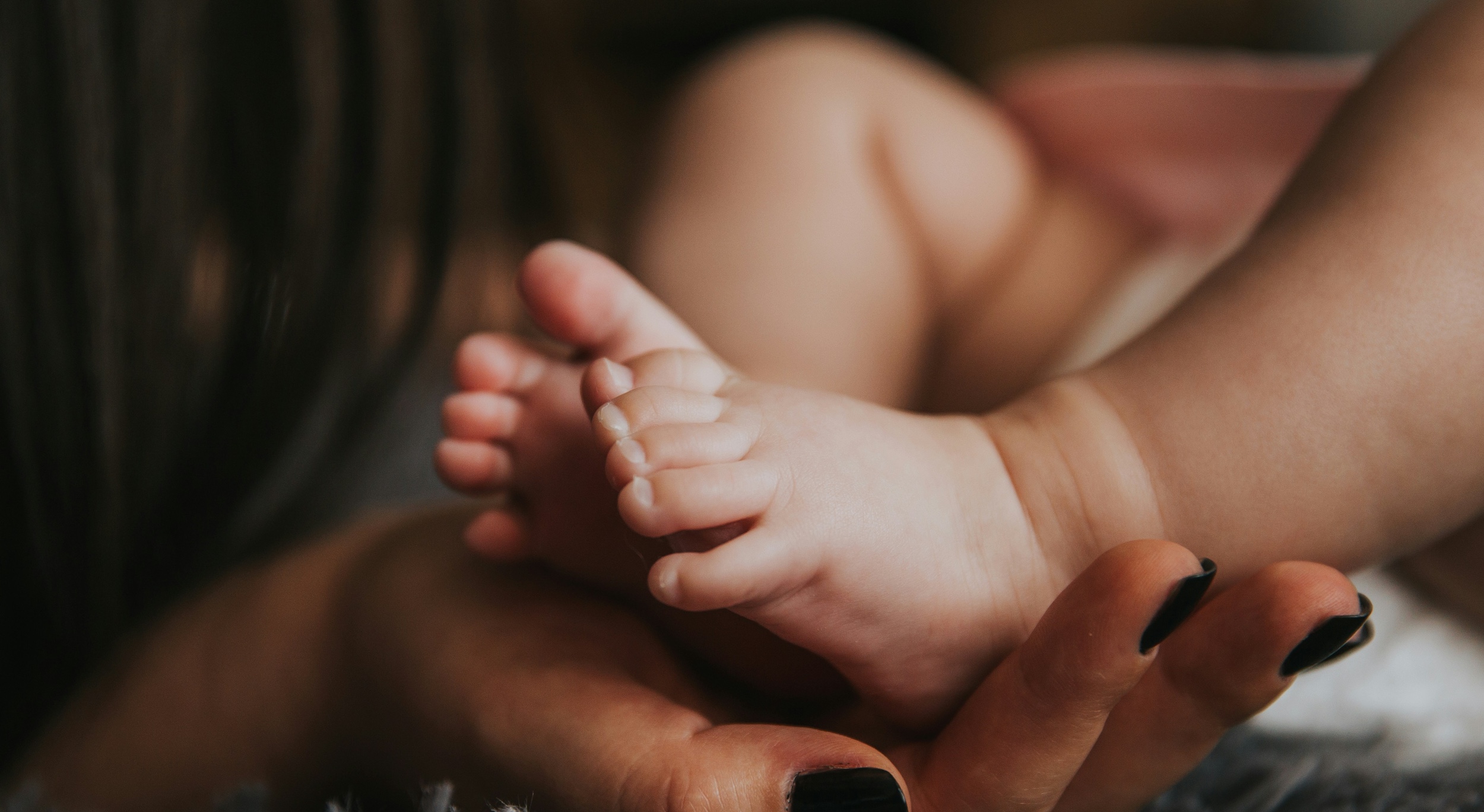 Adult hands gently cradling newborn baby feet